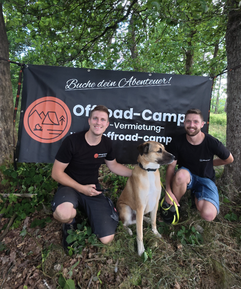 Michael und Marvin, Gründer von Offroad Camper, mit Hund vor dem Firmenbanner