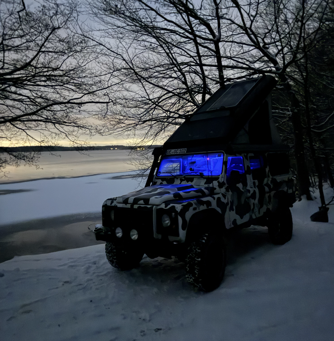 Land Rover Defender im Winter am zugefrorenen See mit blau beleuchtetem Innenraum